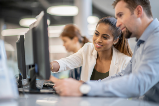 man and woman sitting at computer screens with woman pointing at screen